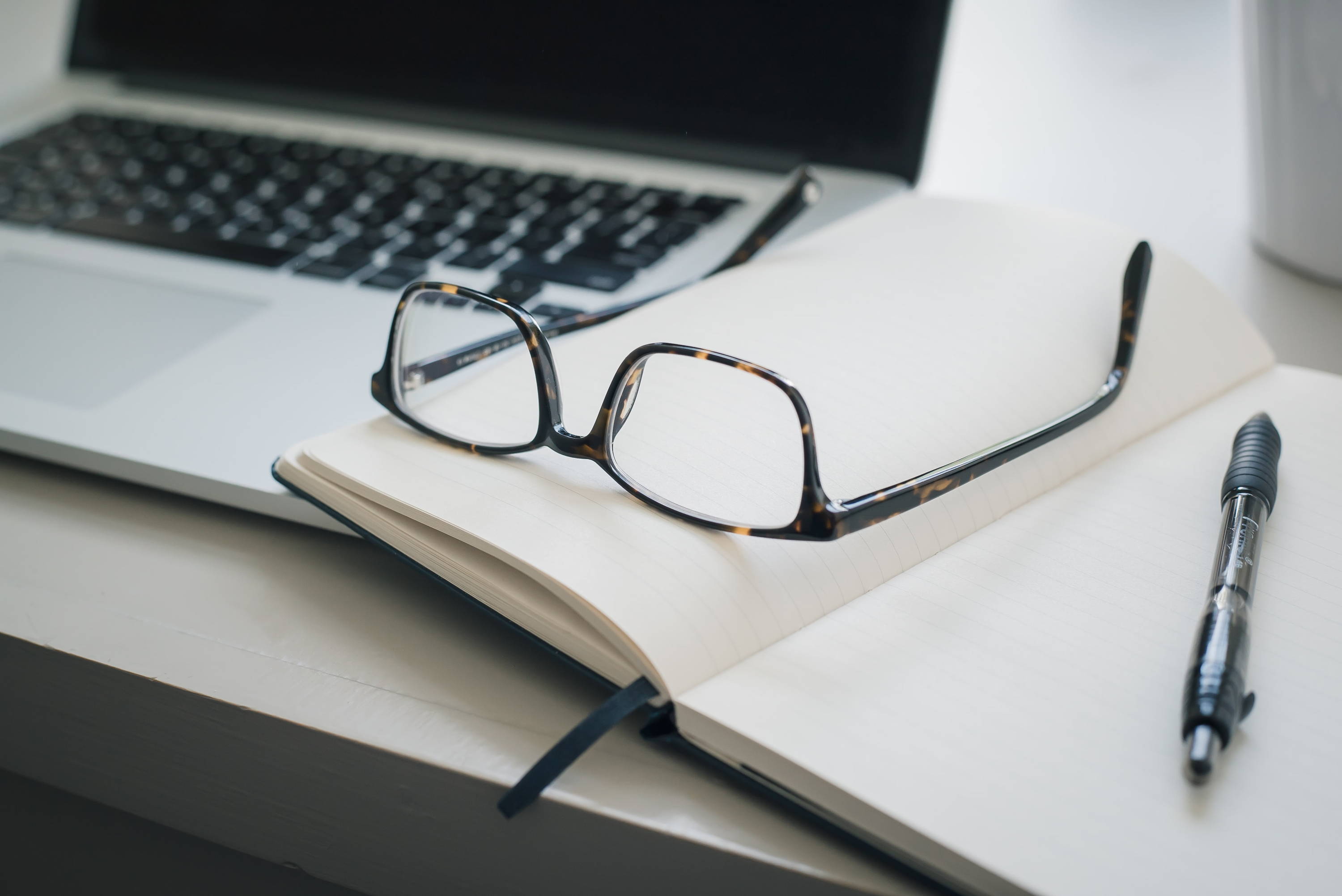 prescription glasses resting on an open notebook and pen placed on a desk