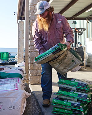 Person lifting a bag of soil or fertilizer outdoors.