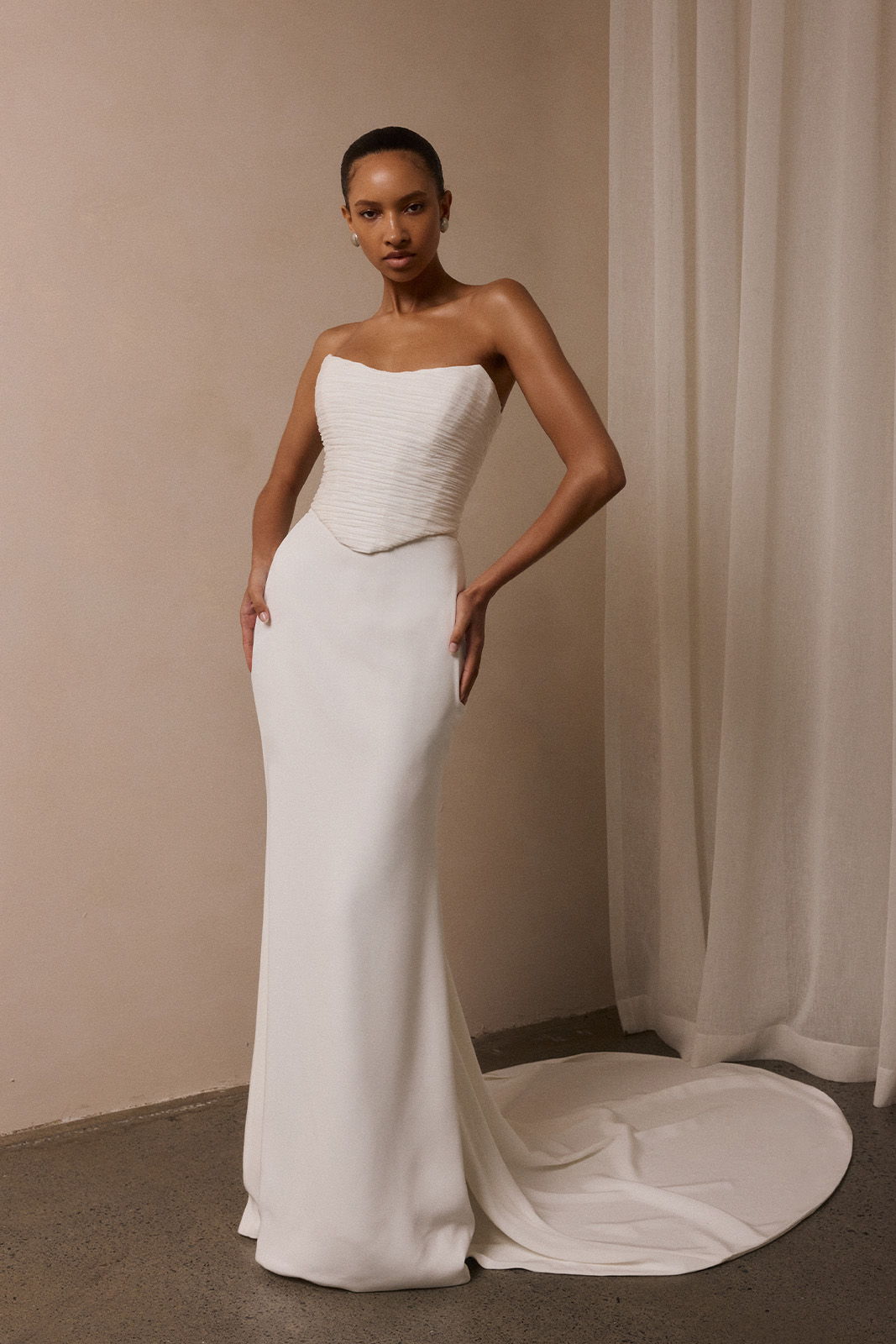 Model in a white strapless gown posing against a neutral background.