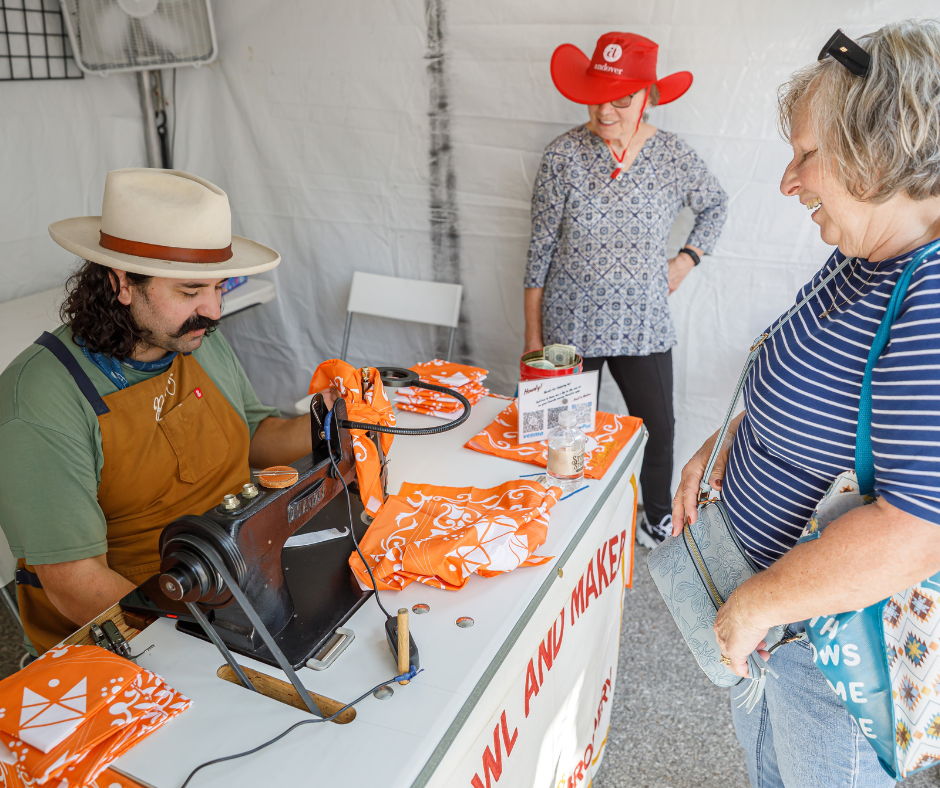 A vendor demonstrating a craft to interested customers at a fair.