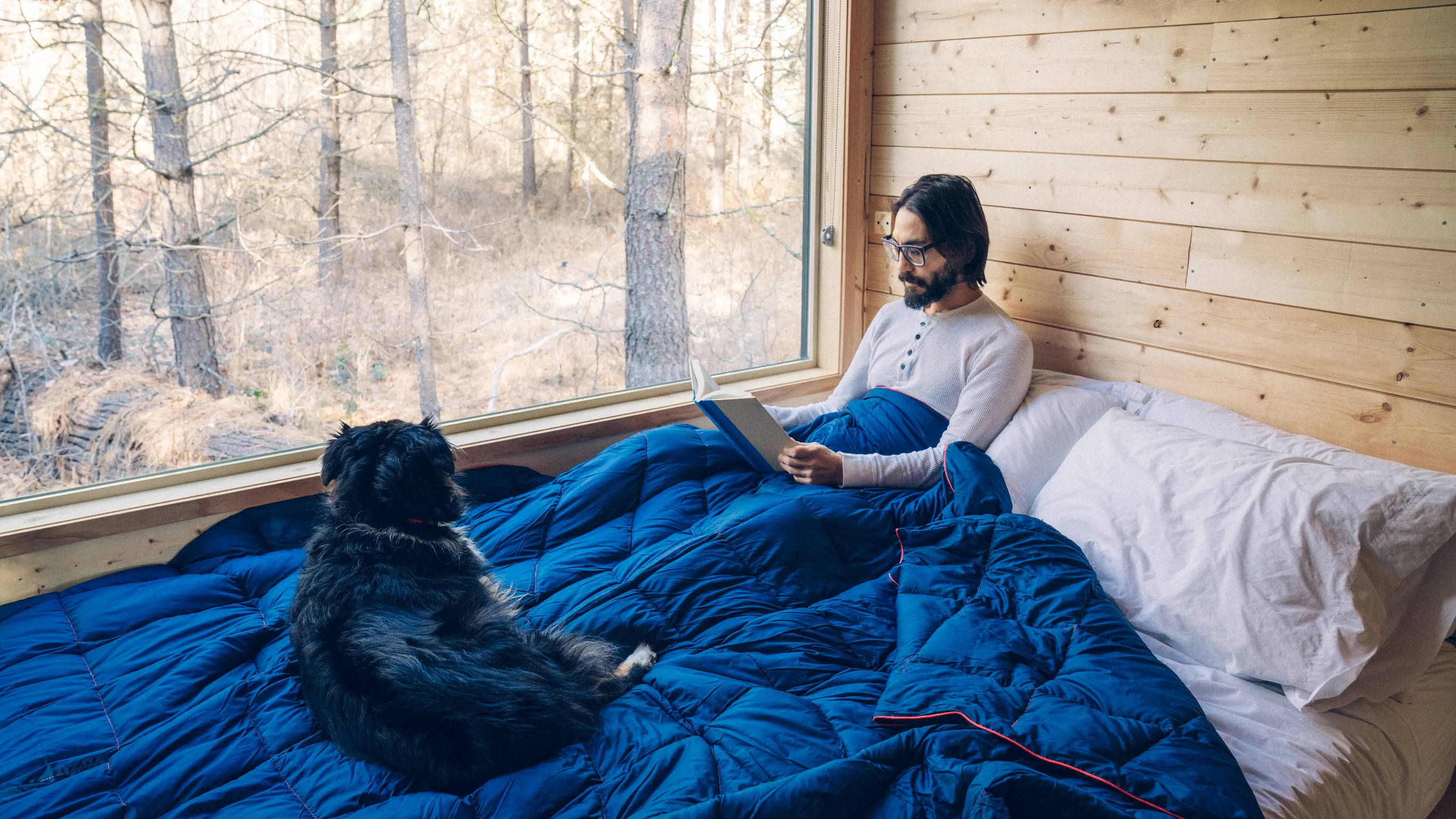 Man reading a book laying under a Rumpl down blanket inside his Getaway House