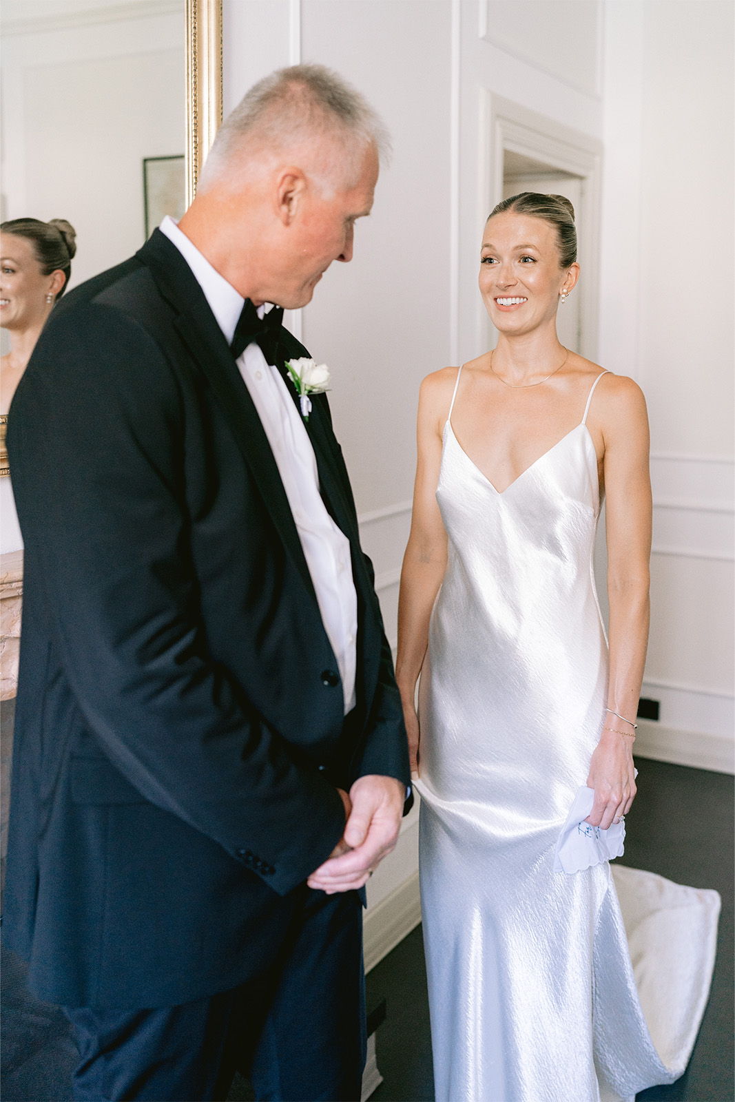 A bride in a satin gown smiles at a man in formal attire.