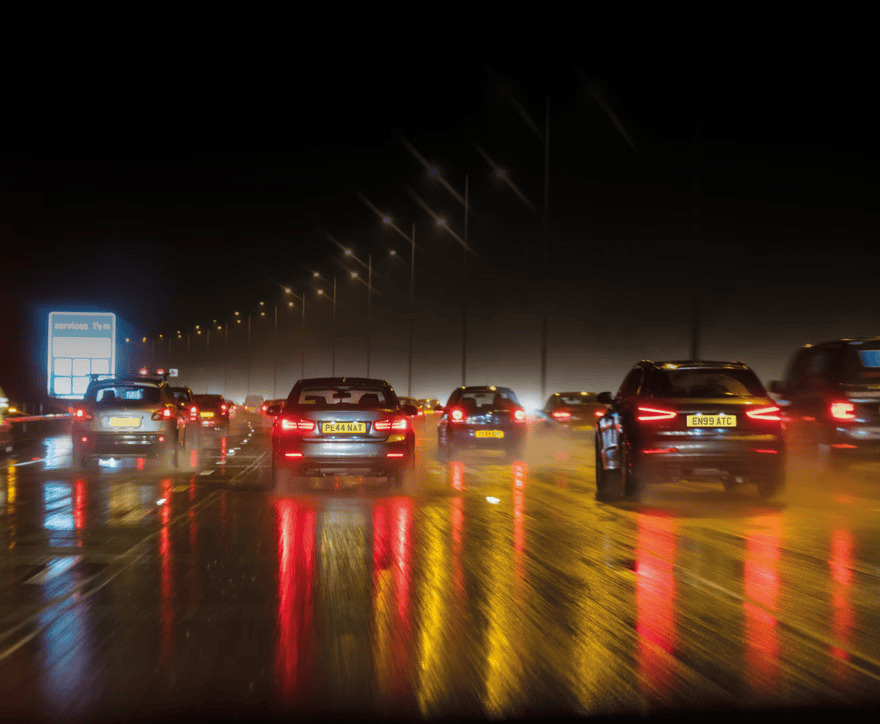 Cars on a wet road at night, reflecting lights in the rain.