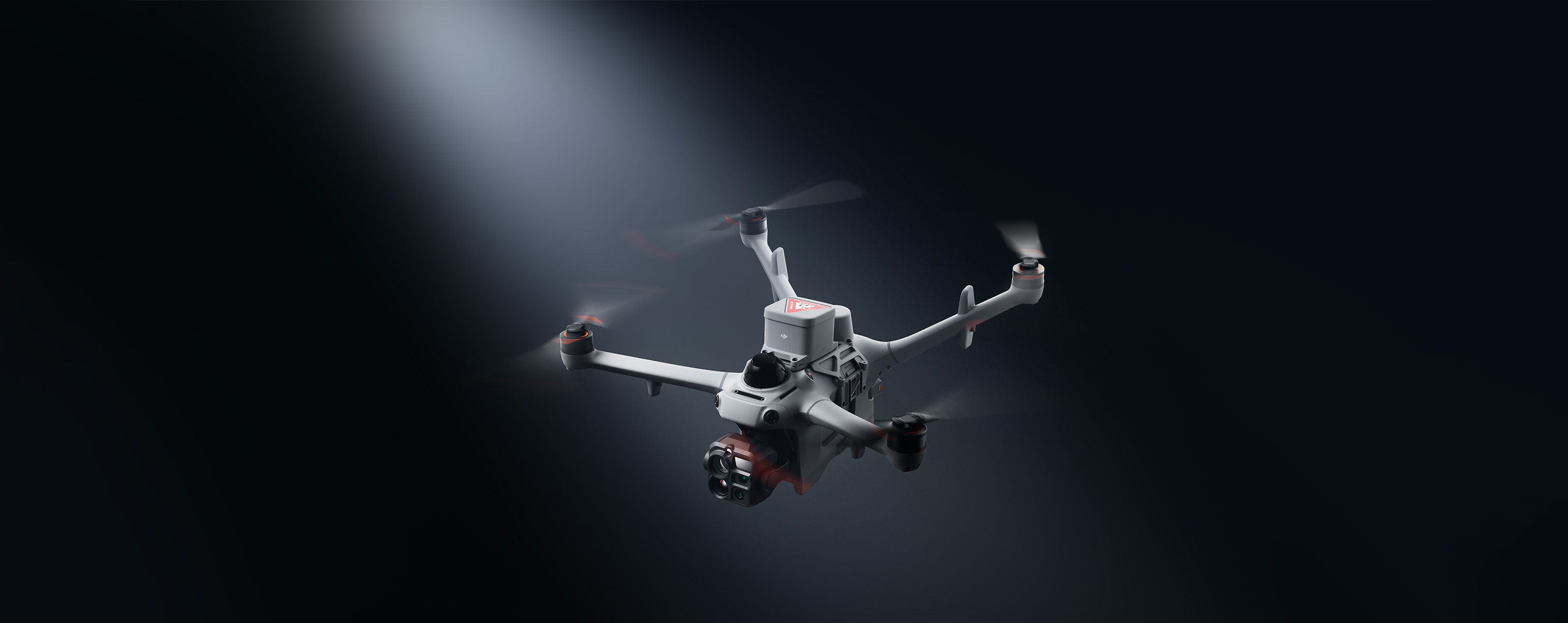 A DJI Matrice 5TD drone flying in a beam of light against a dark background.