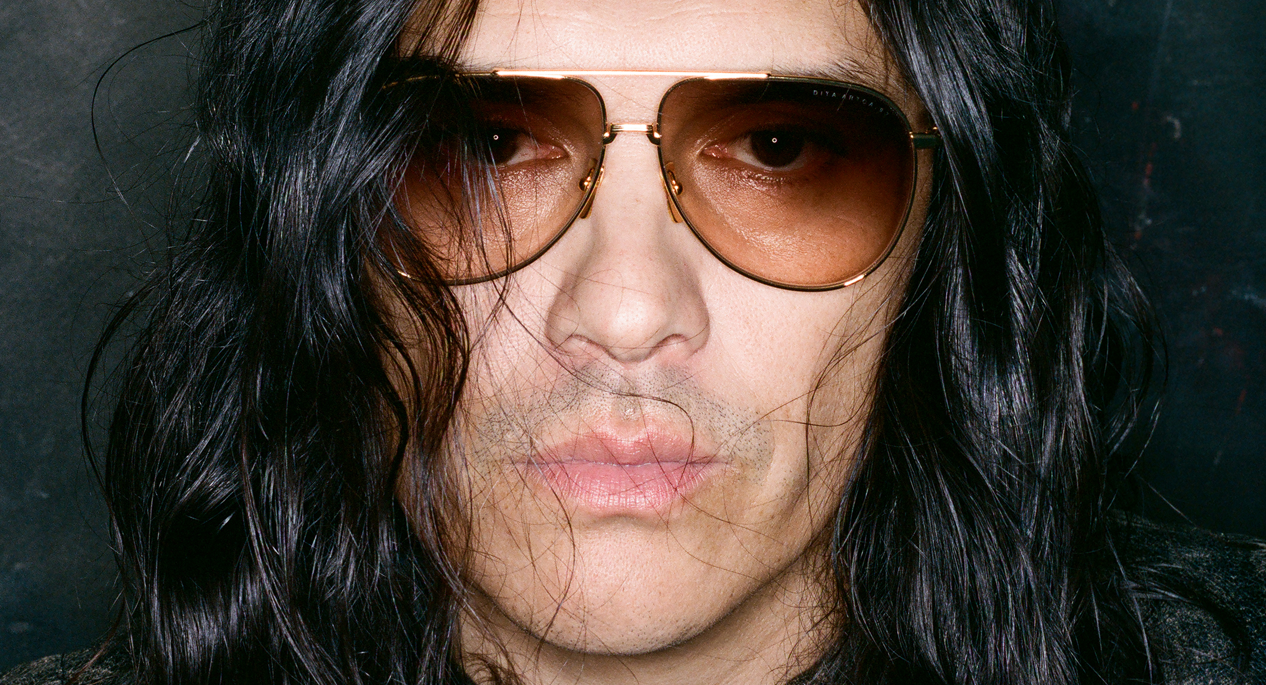 Person with long dark hair wearing sunglasses, staring directly at the camera.