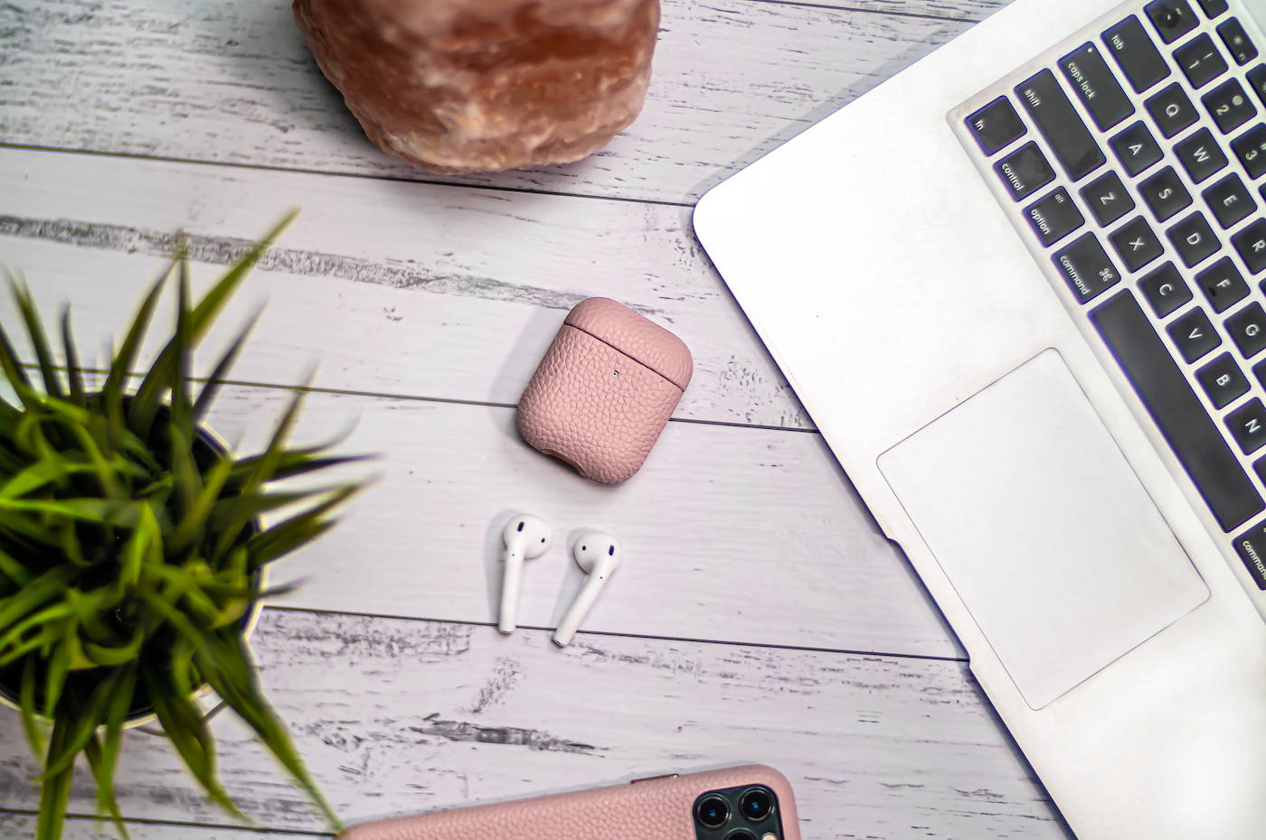 pink genuine leather airpods case laying flat on grey wooden table with macbook air laptop