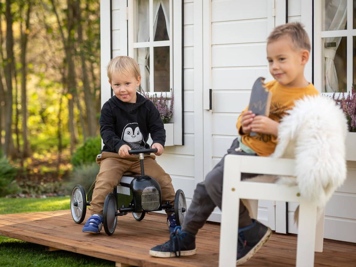 Two boys playing on a wooden playhouse porch with forest on the background by WholeWoodPlayhouses