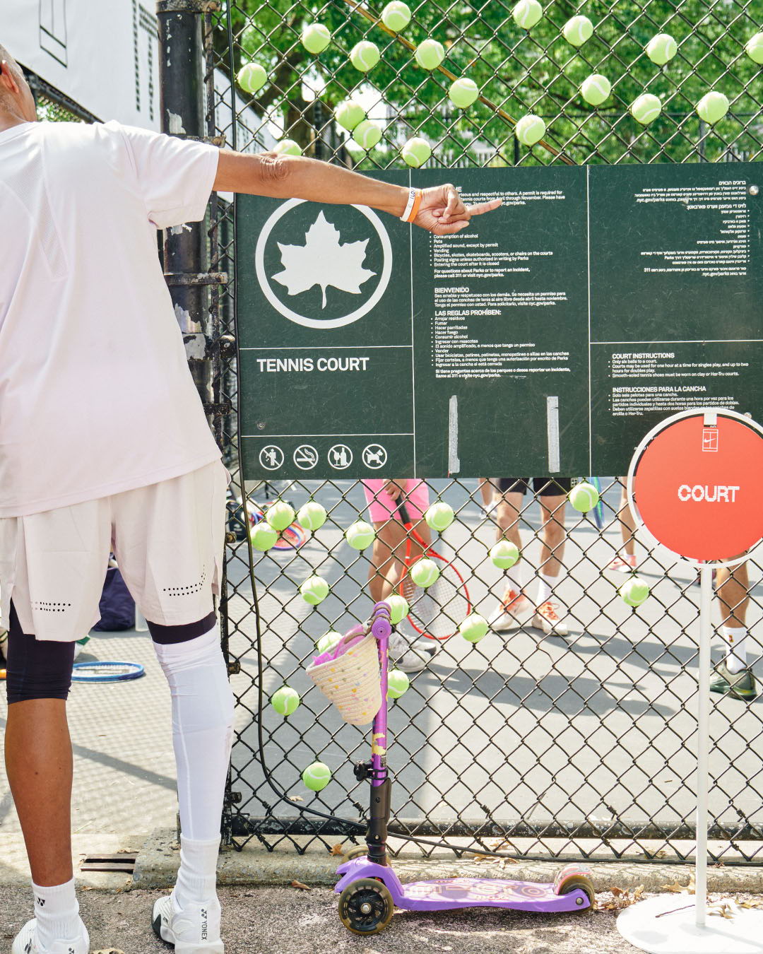 Person pointing at tennis court rules with tennis balls in the background.
