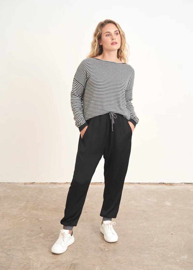 A model wearing a pair of black satin trousers with silver metallic cuffs and waist tie with a black an white striped jumper