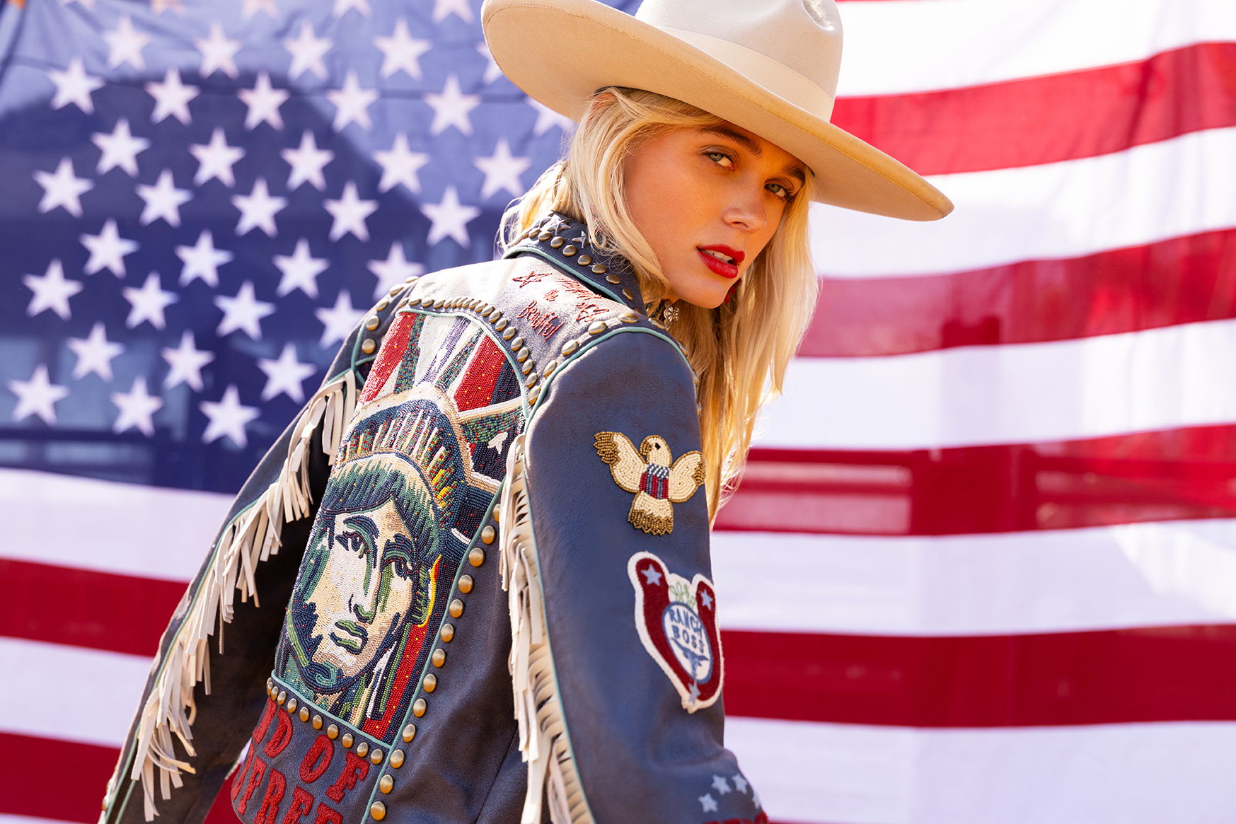 Haley wearing the Lady Liberty Biker Jacket posed in front of an American flag wearing a vintage Double D Ranch hat.