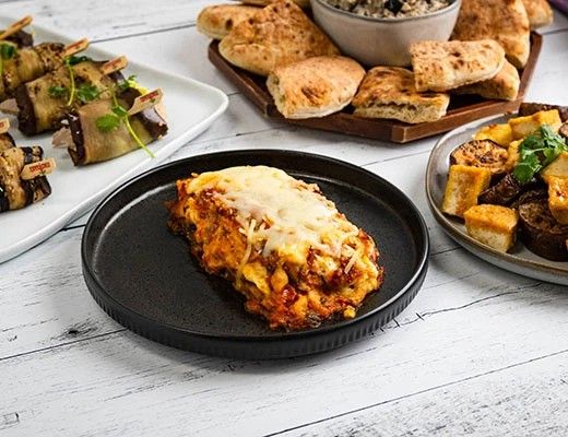 A plate of lasagna with sides of vegetables and bread.