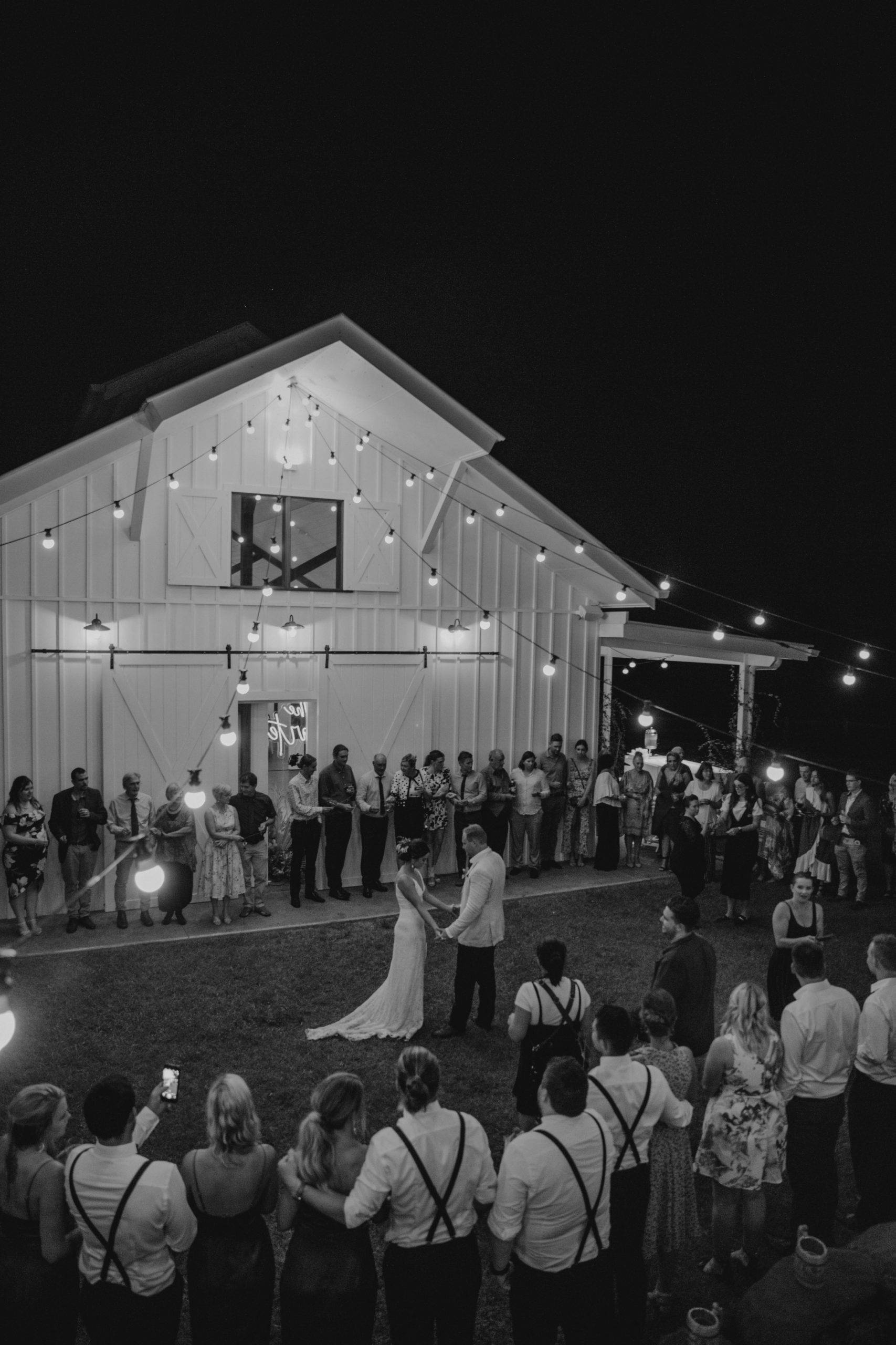Wedding guests in a circle outside a white barn bride and group dancing in the middle