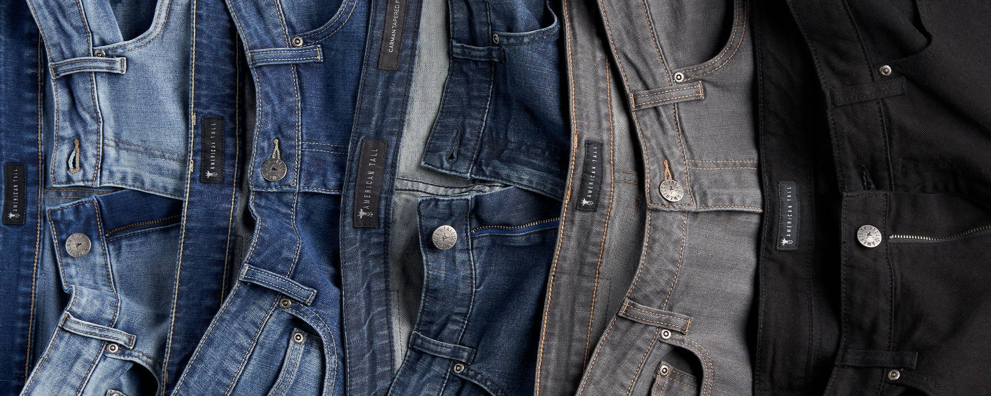 Tall men's jeans layered over top of each other arranged from light blue to black.