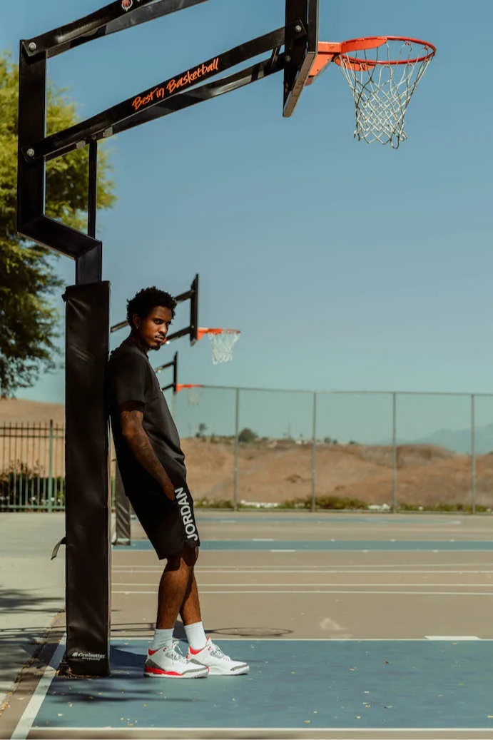 male model in aj3 retro og fire red standing underneath basketball hoop