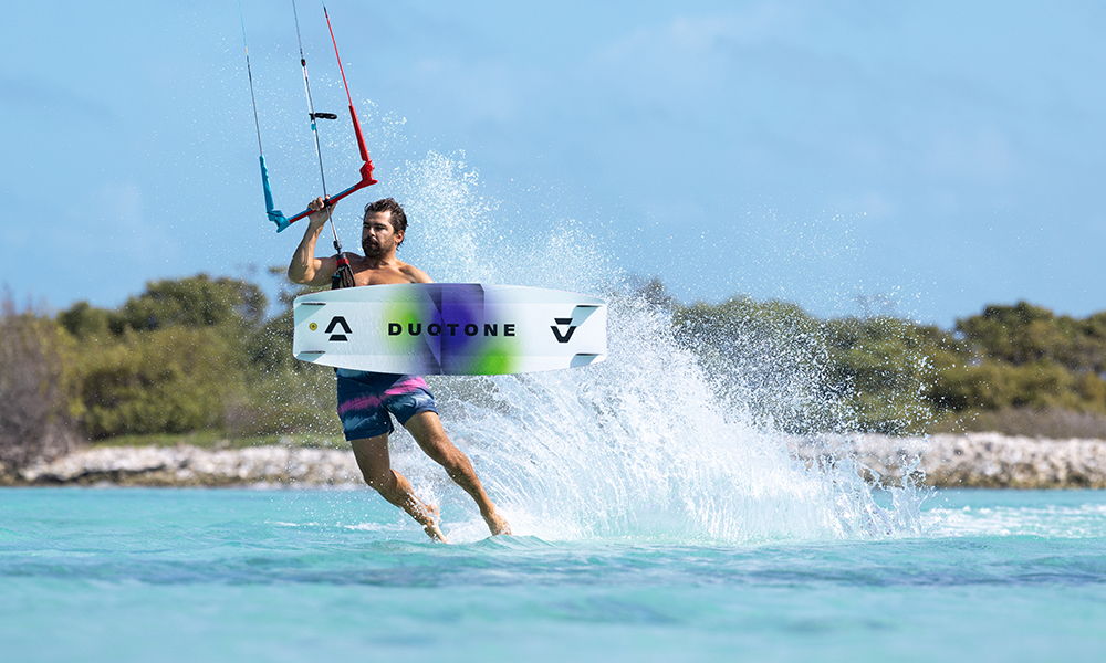 Un kitesurfeur surfant sur une vague dans une eau d'un bleu limpide. avec une Duotone Select SLS 2026