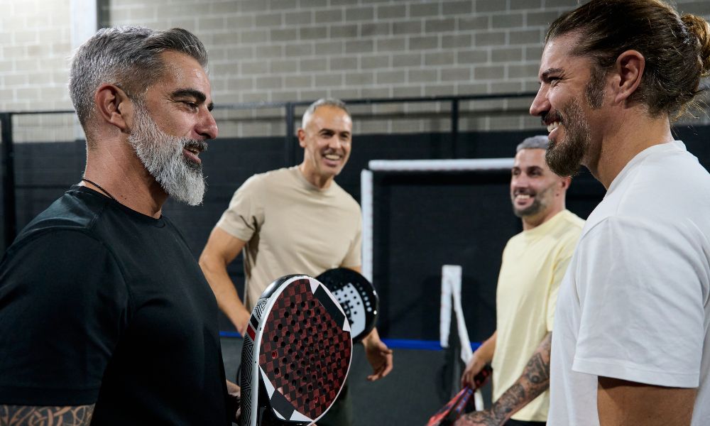 Four men chatting and smiling while holding paddles in a sports setting.