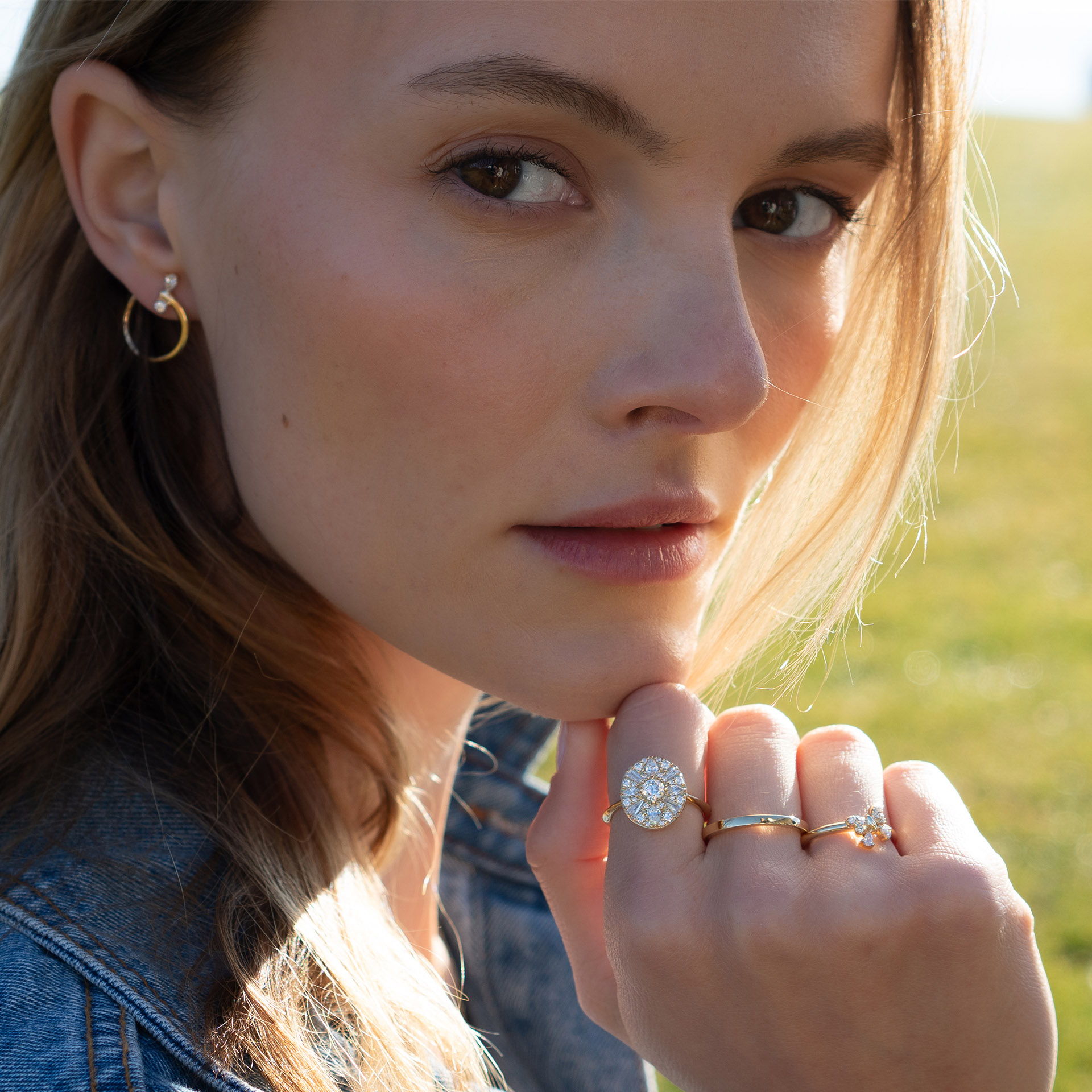 A woman wearing jewelry, looking thoughtfully at the camera outdoors.