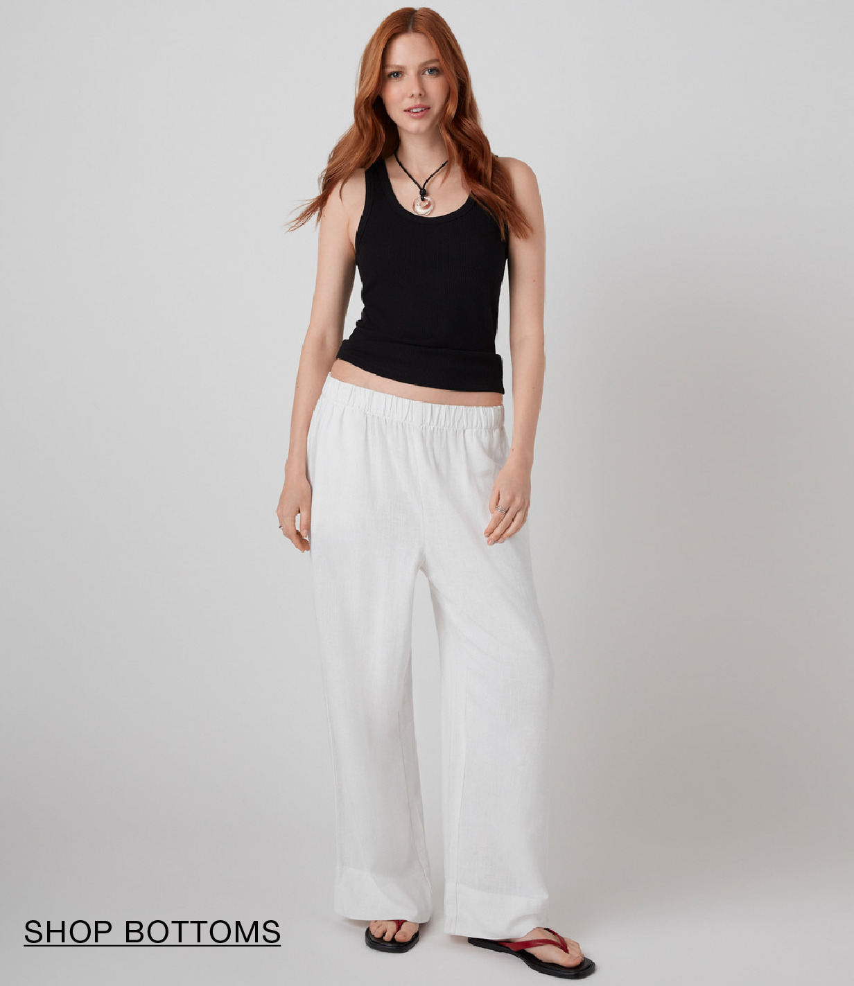 Model wearing a black tank top and white pants, standing and smiling.