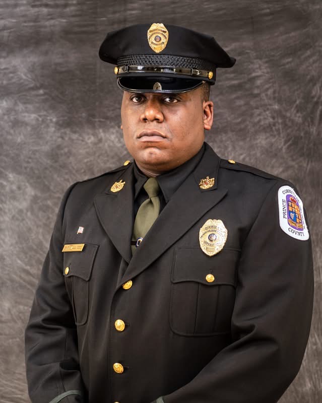 A police officer in uniform, standing against a neutral background.