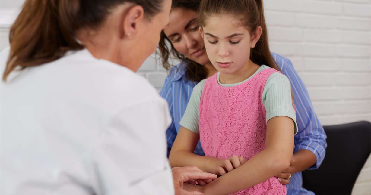 Child sitting on her mother’s knee. They’re discussing doing an allergy test. 