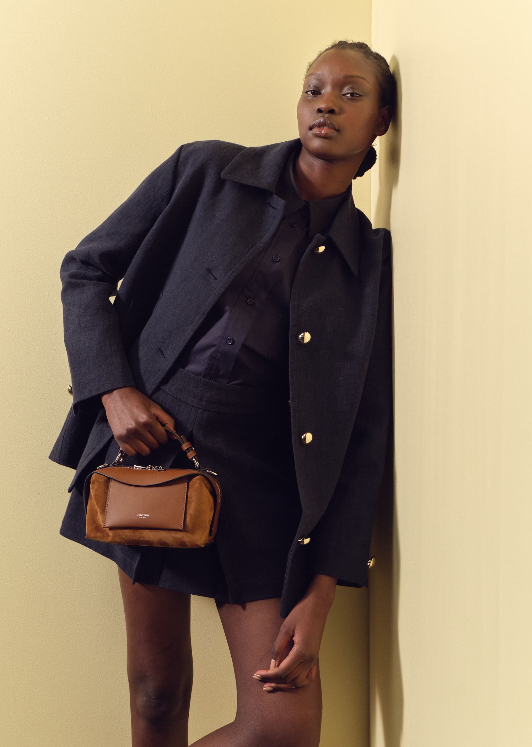 A model in a stylish outfit poses against a yellow wall.