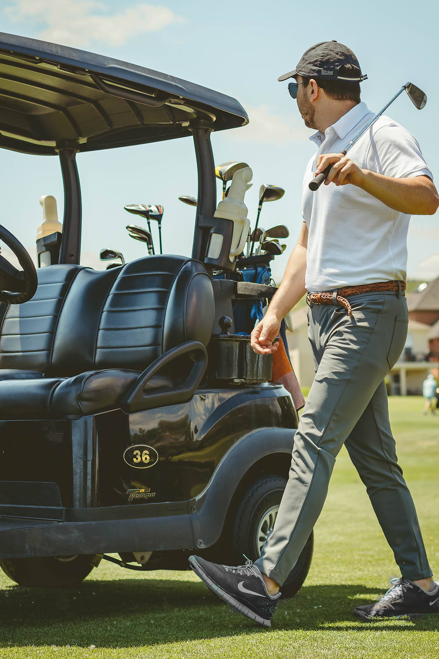 Male Golfer walking to his golf cart wearing white polo shirt with Gray Performance Pants from Under510.com holding a putter over his shoulder