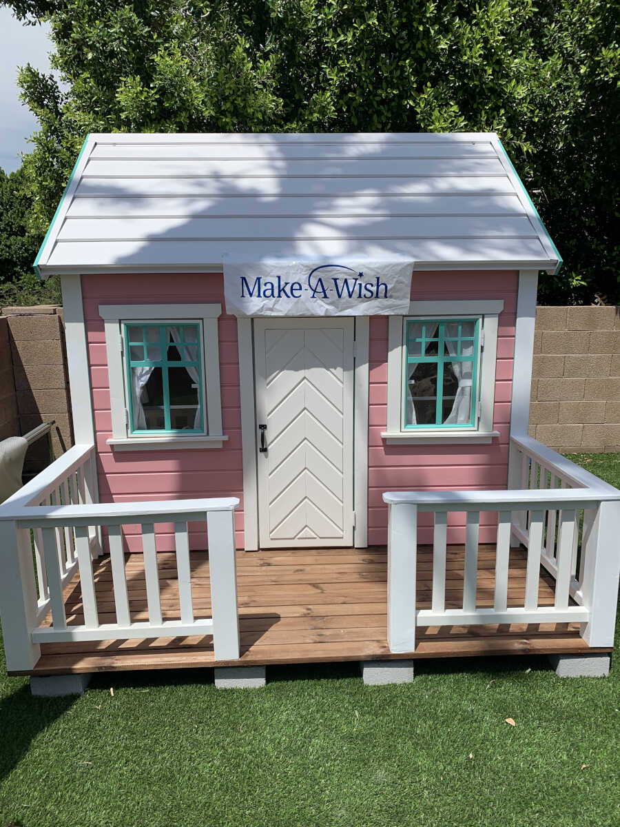 Pink Wooden Playhouse Unicorn With White Metal Roof, a terrace with white railing and white Door in the backyard By WholeWoodPlayhouses 