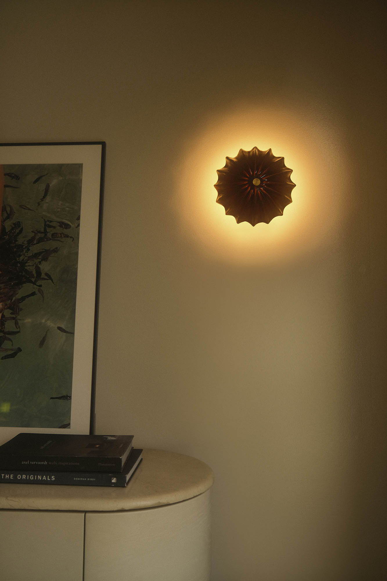 Hexacorallia tenmoku wall light illuminating a plain wall, with books nearby.