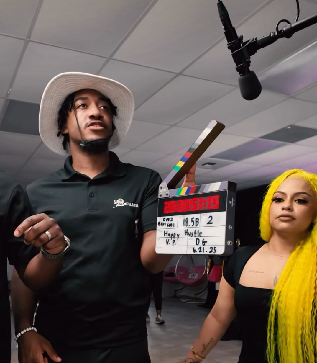Two individuals on a film set with a clapperboard and microphone for the Happy Hustle Show