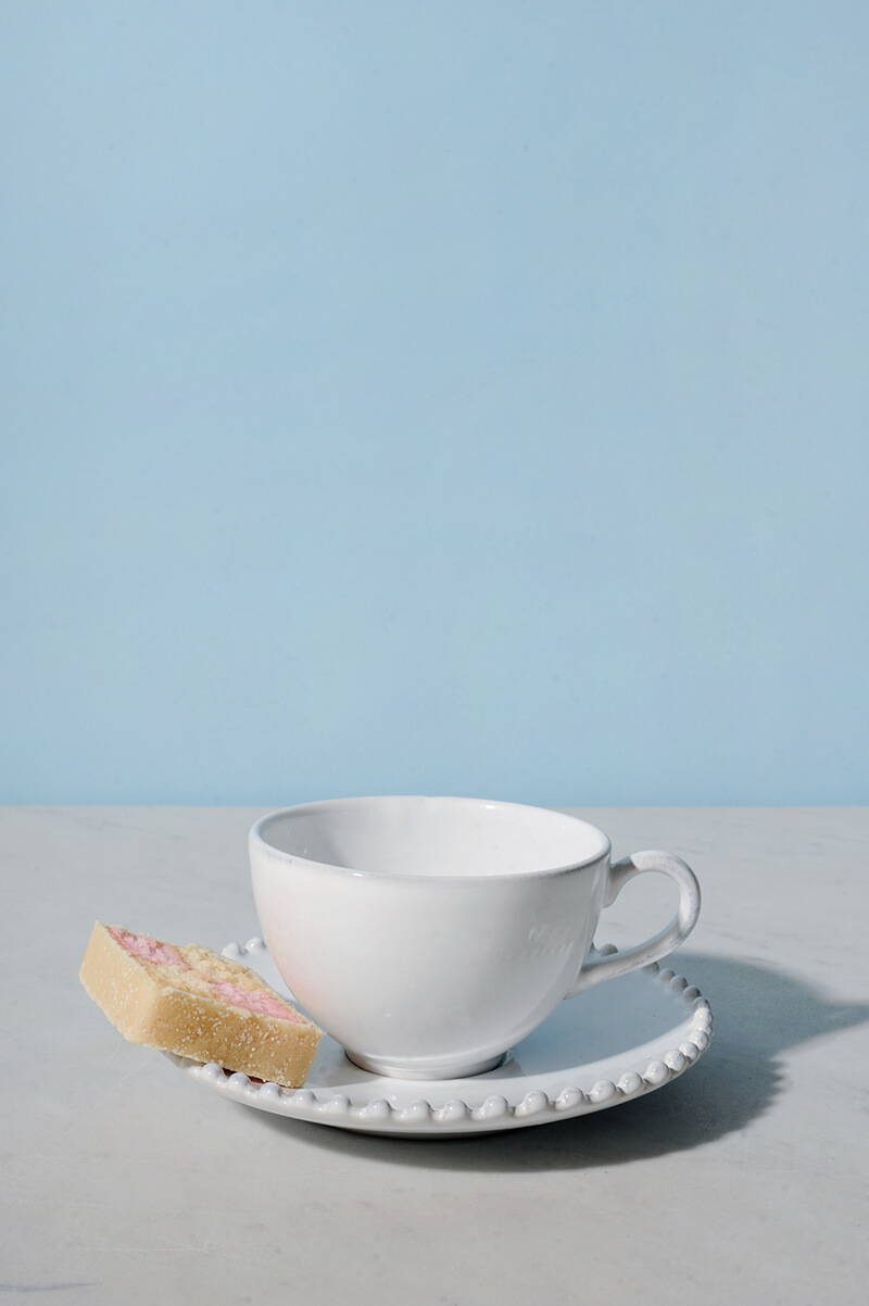 A Pearl White tea cup and saucer with a slice of Battenberg cake.