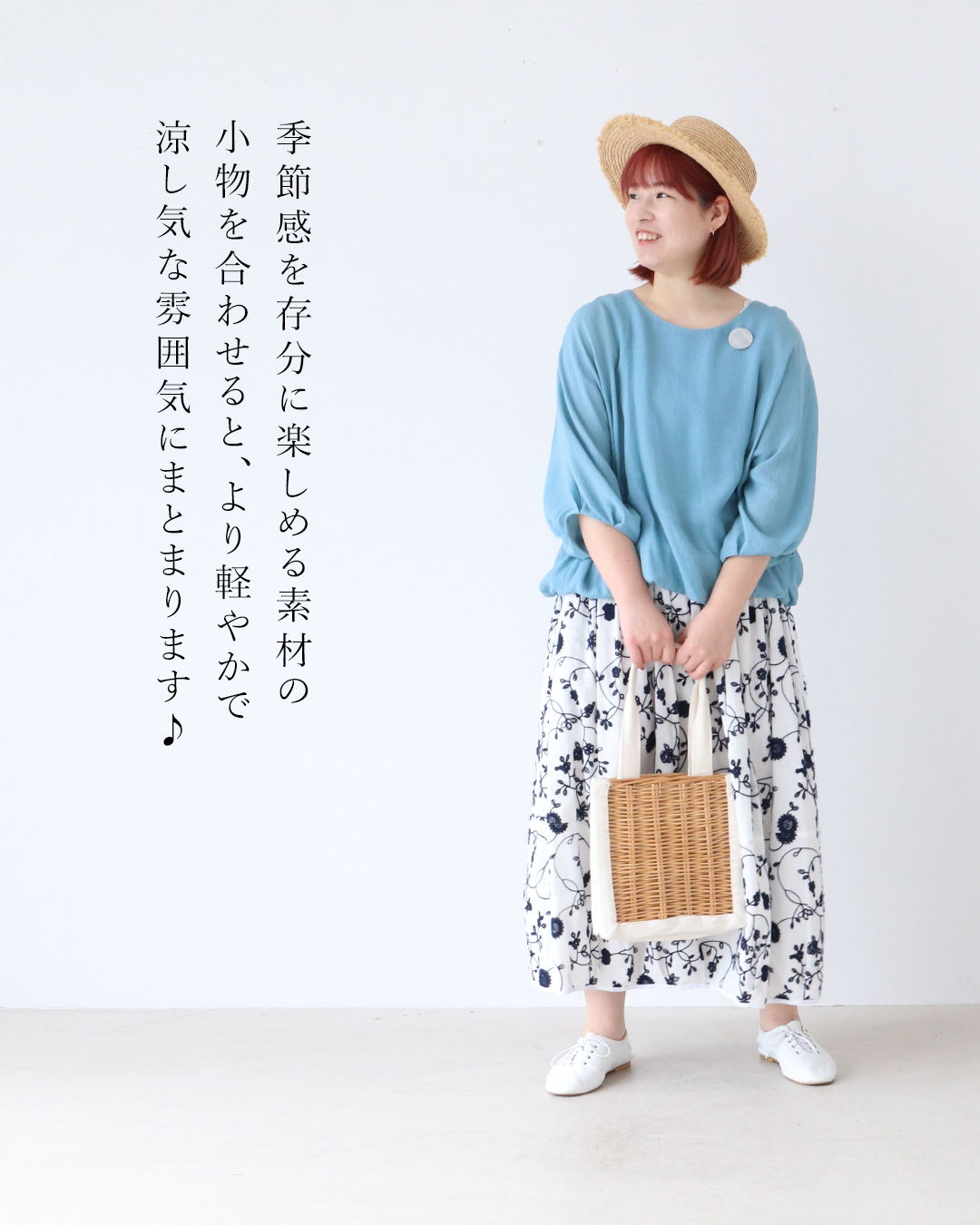 Woman wearing a blue top and floral skirt, holding a bag, smiling.