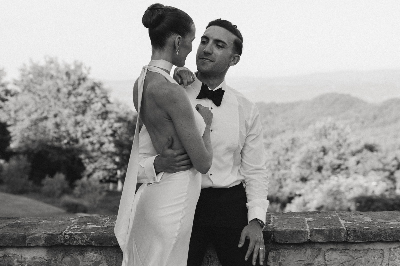 A couple embracing in formal attire against a scenic background.