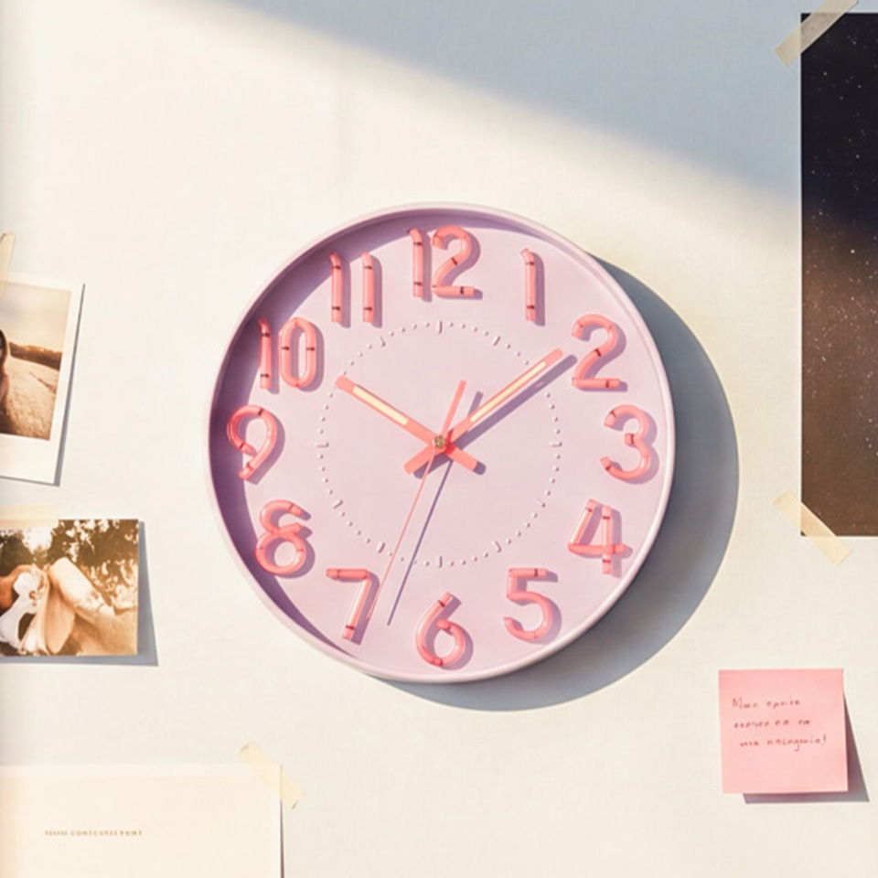 A pink wall clock with large numbers hanging on a wall.