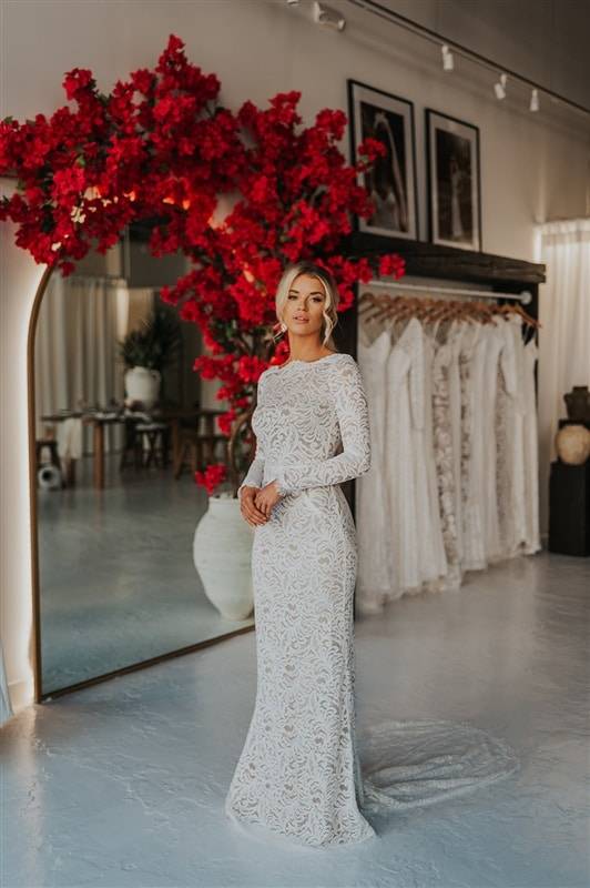 Mariée portant une robe en dentelle à manches longues avec miroir d'arc et bougainvilliers rouges 