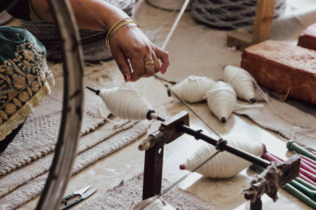 Eine Frauenhand spinnt Wolle für einen Teppich
