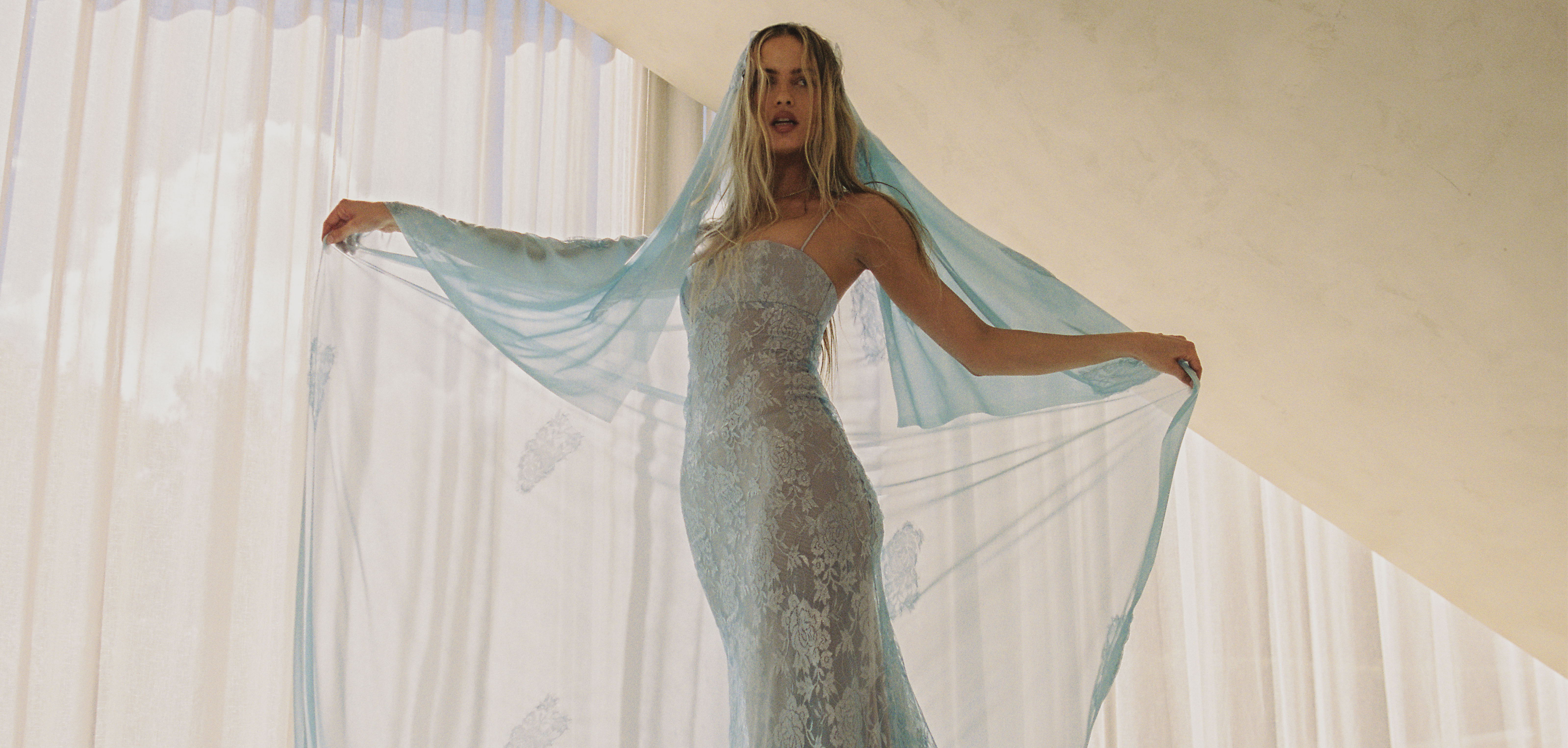 Woman in a flowing blue gown with a veil, posing elegantly indoors.