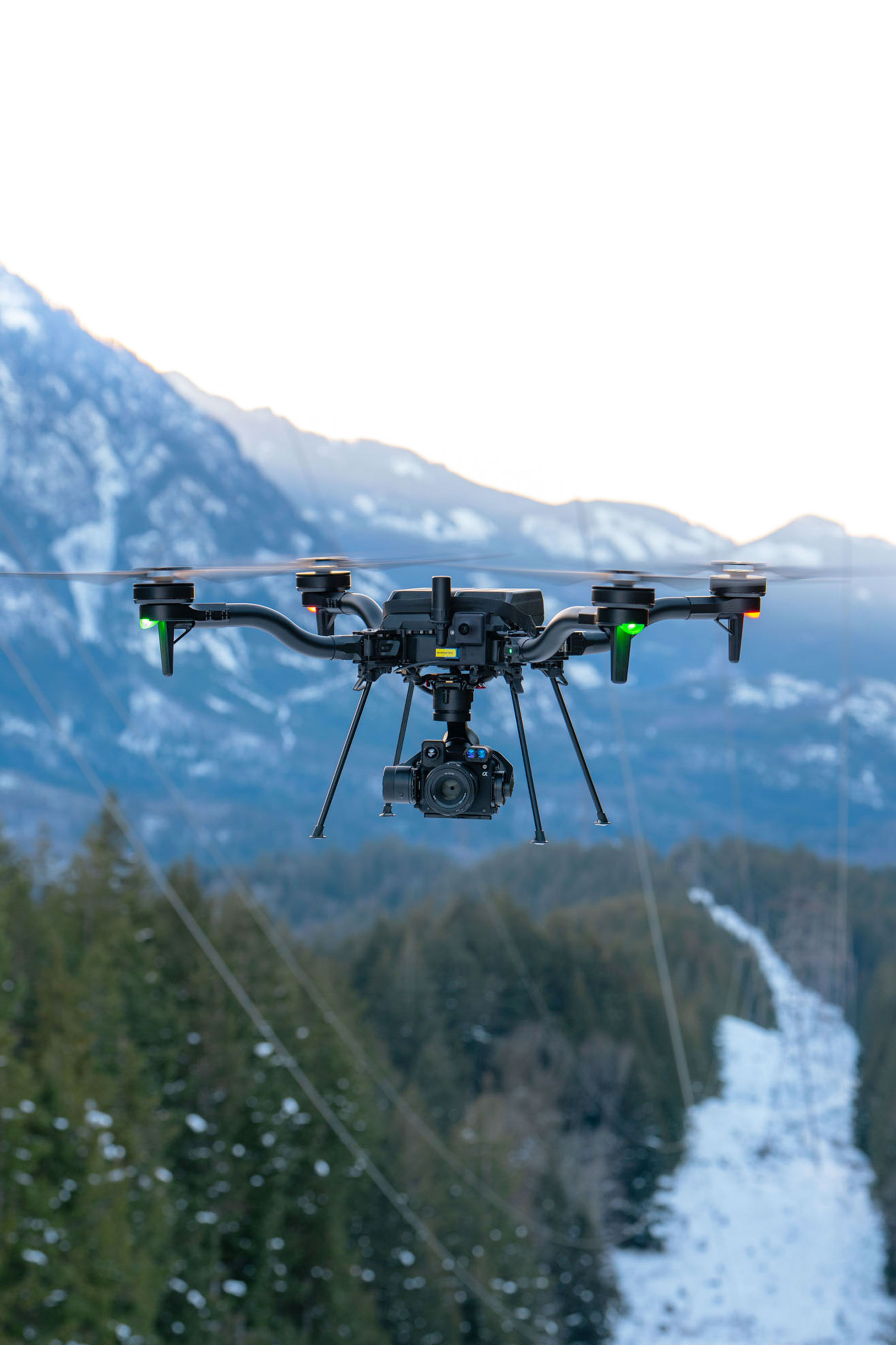 Un drone Freefly Astro volant au-dessus d'un paysage enneigé avec des montagnes en arrière-plan.