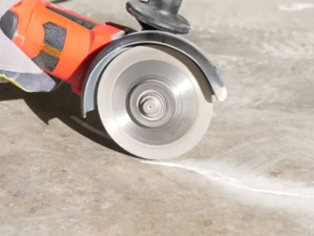 Using a grinder and diamond blade to widen cracks in the floor, preparing it for material filling.