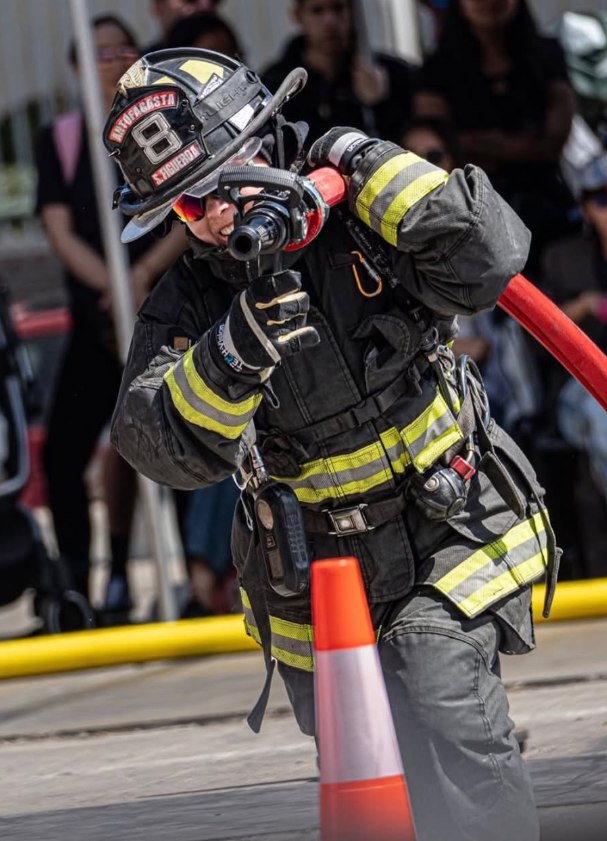 Firefighter aiming a hose, with crowds in the background.