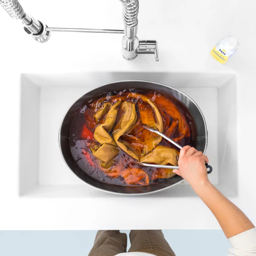 Person using tongs to remove fabric from a bowl of dye in a sink.