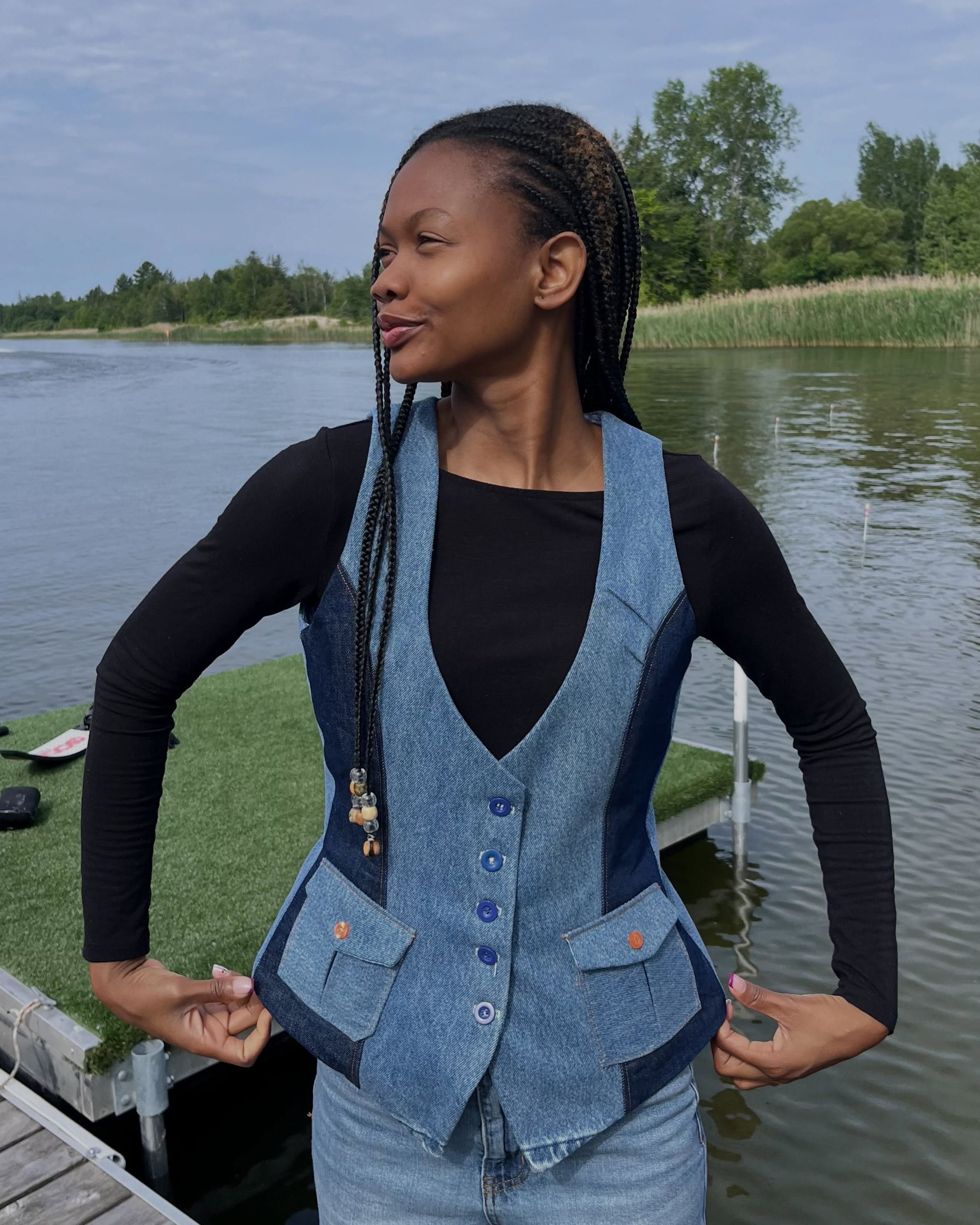 A person in a denim vest poses by a serene lake.