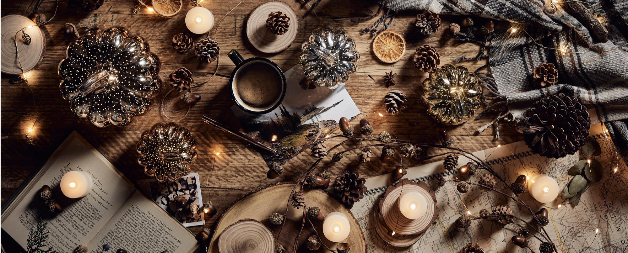 Autumn pumpkins, LED candles and garlands with books, drinks and pinecones on a wooden table.