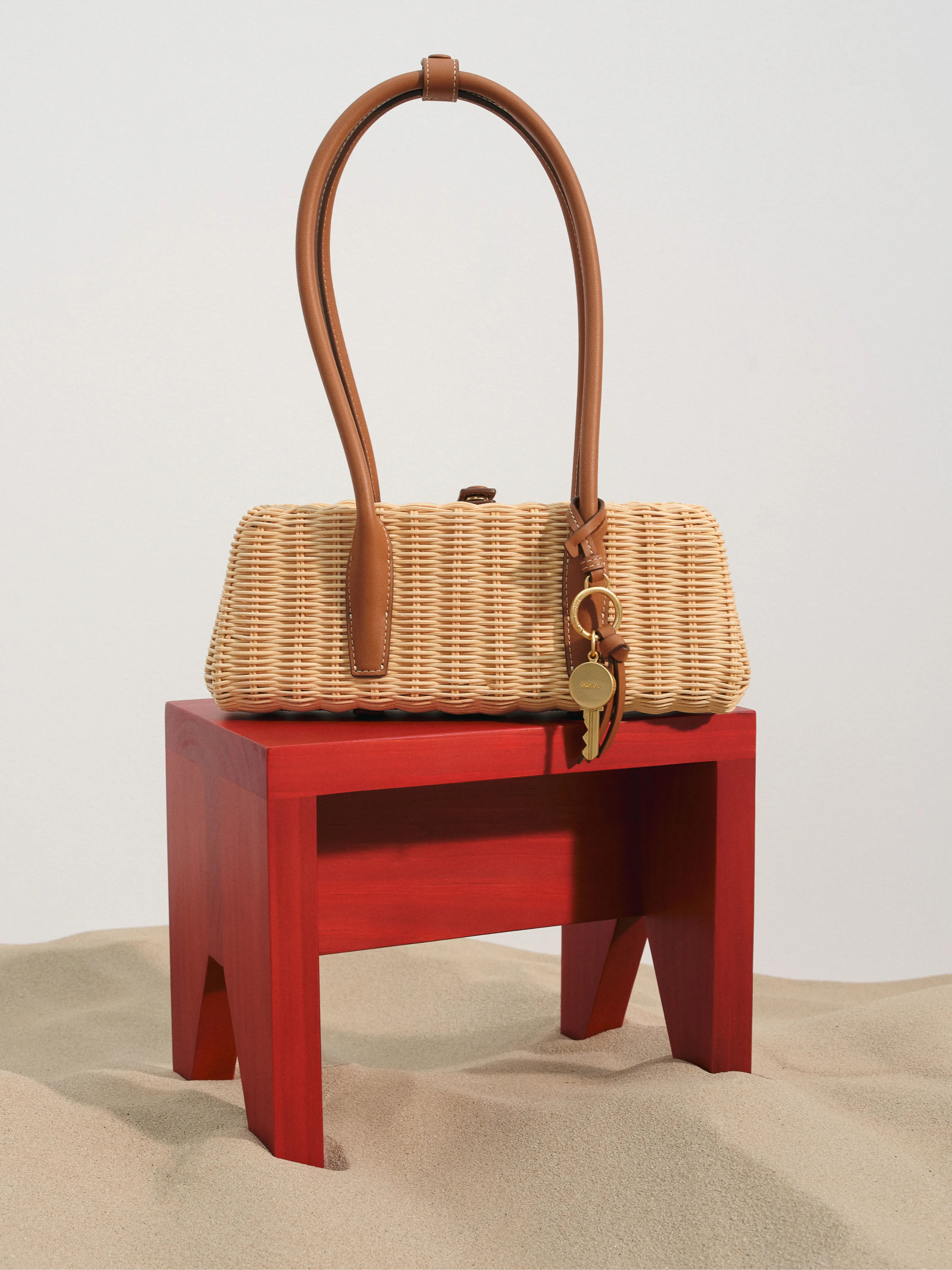 A woven handbag on a red stool in a sandy environment.