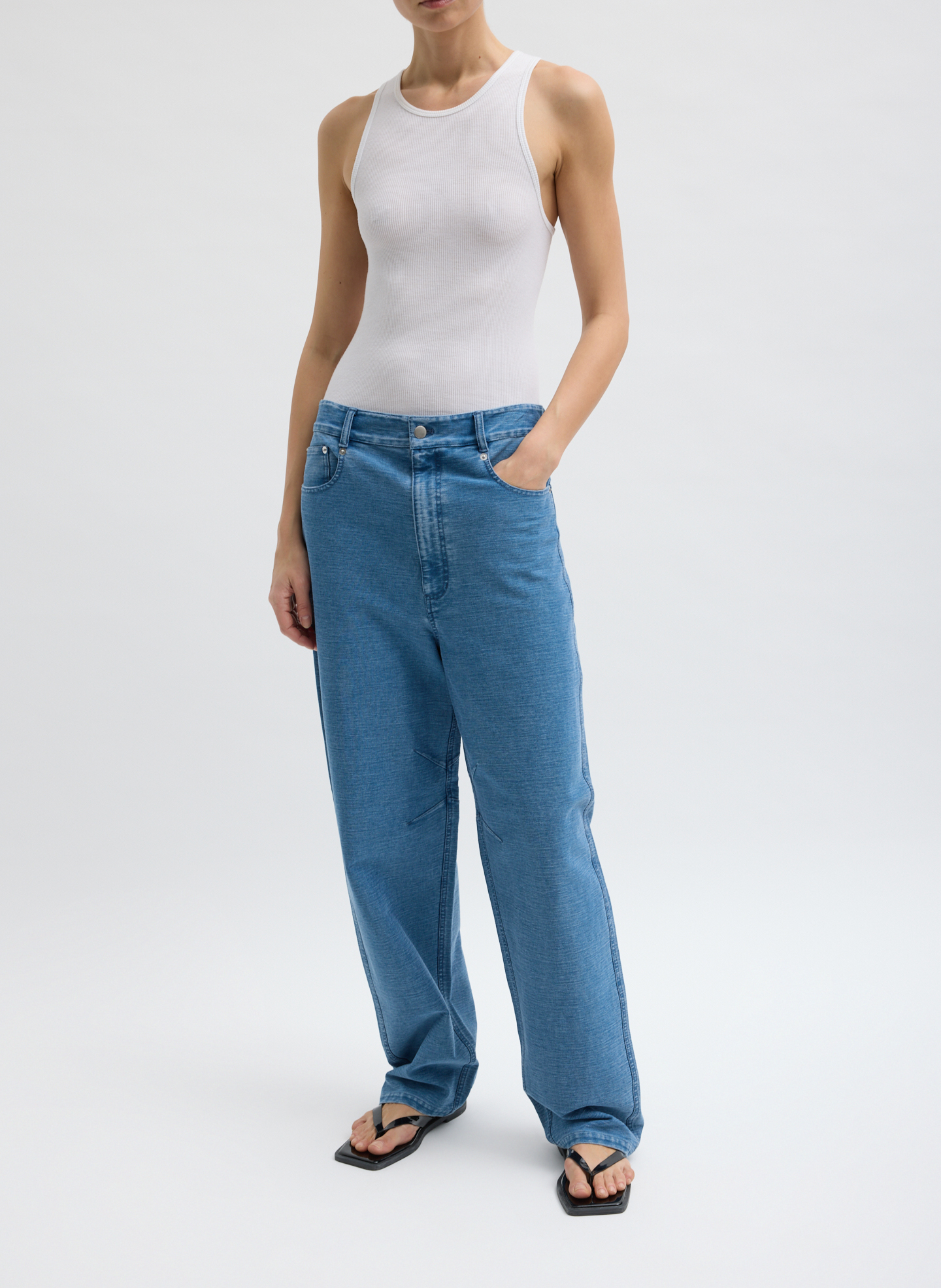 A person wearing a white tank top and blue jeans.