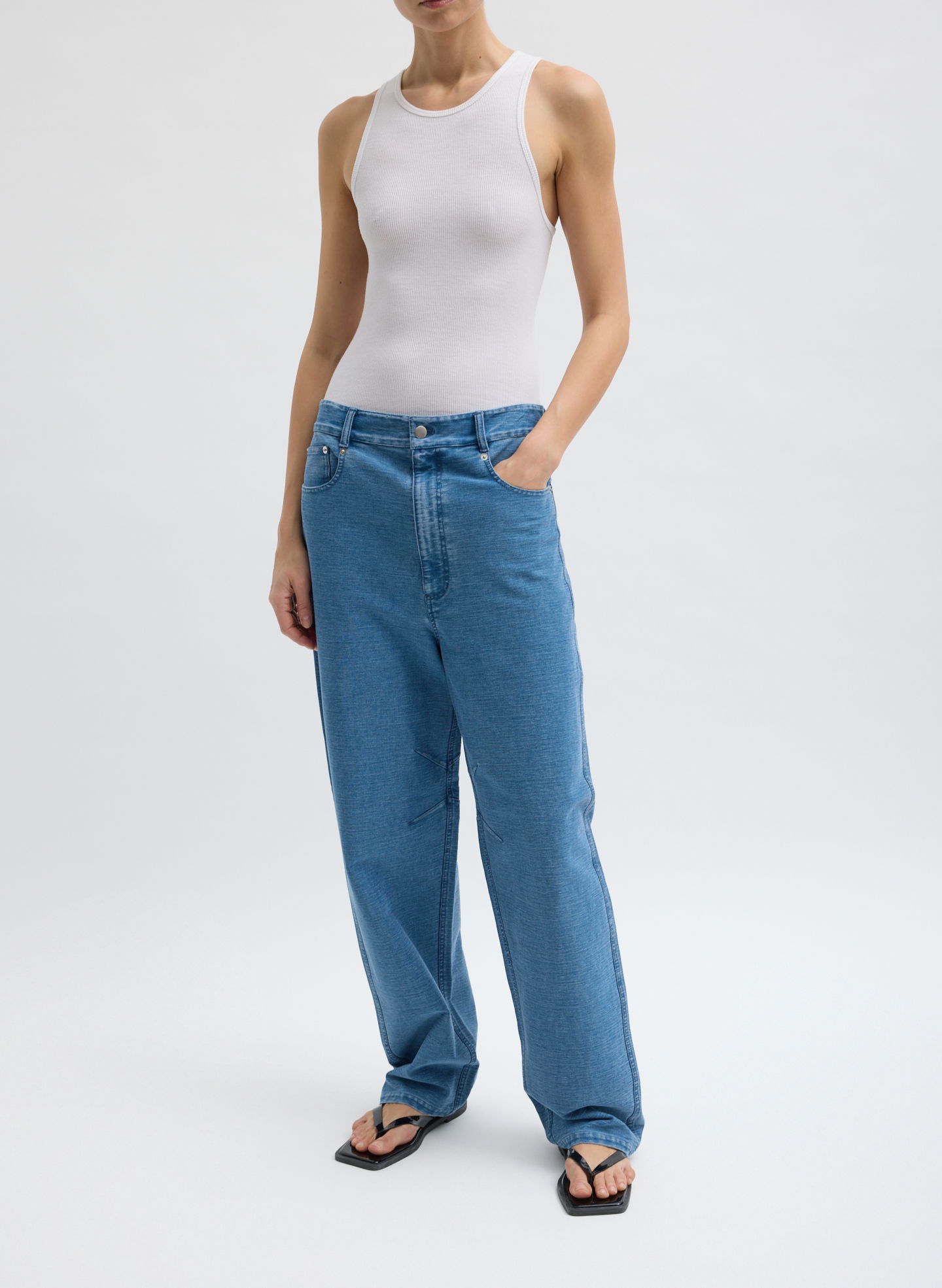 A person wearing a white tank top and blue jeans.