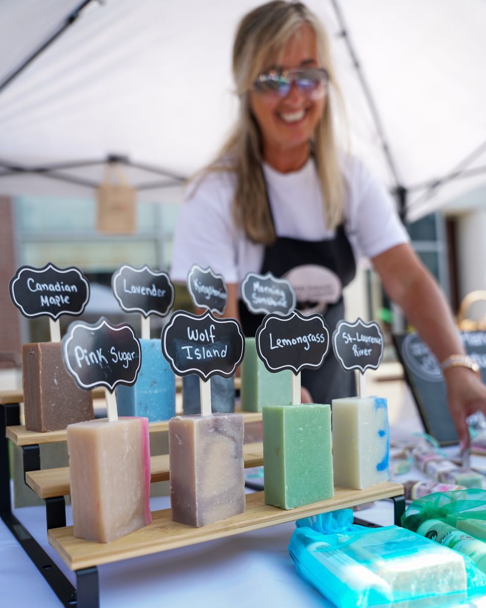 A vendor displays colorful soaps at a market under a tent.