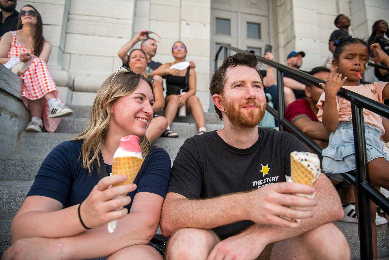 A couple enjoying ice cream on steps with a crowd in the background.