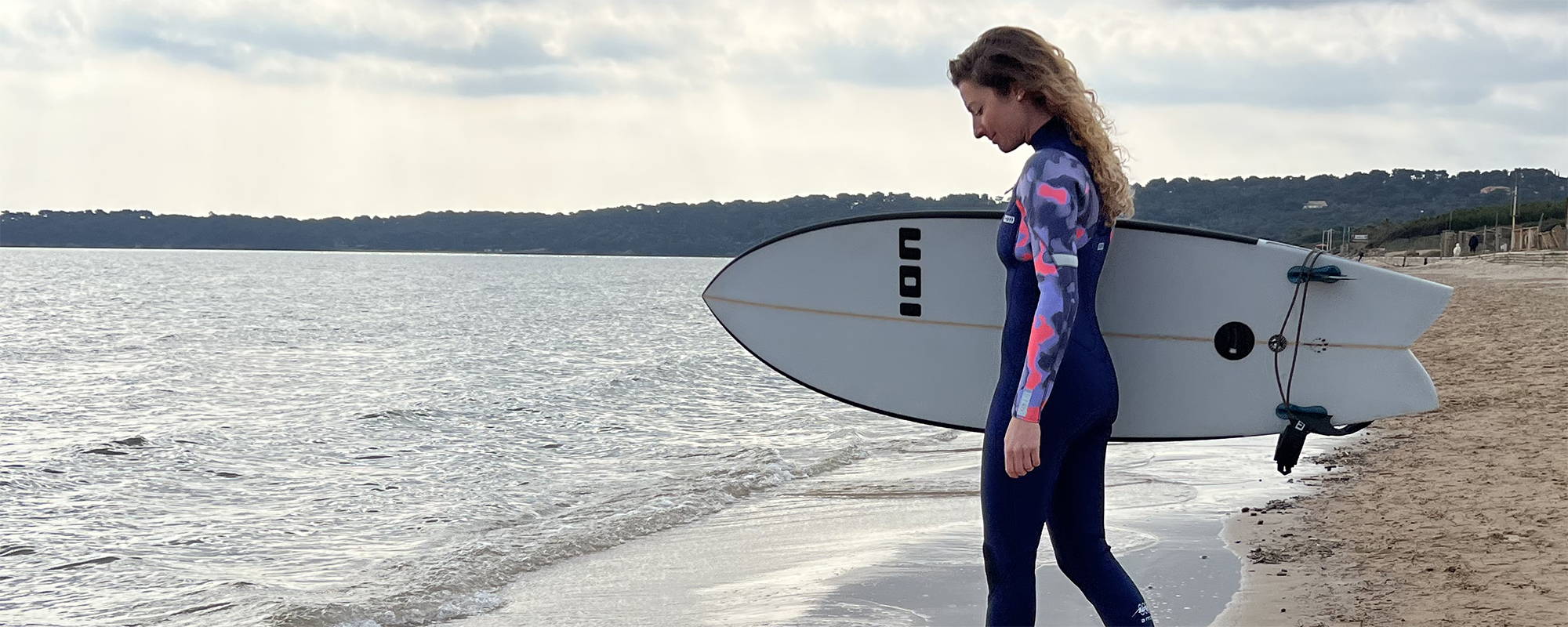 Une fille en combinaison neoprene ION  avec un surf sur une plage