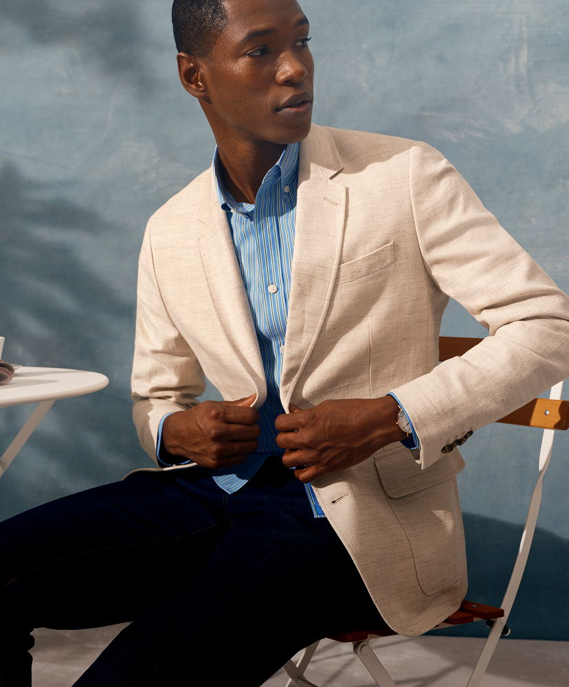 Man in a light blazer and blue shirt, seated beside a table.
