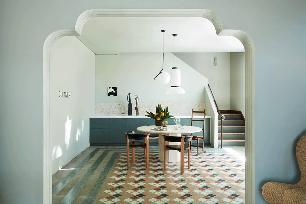 Foyer of the CULTIVER office. Bordered checkerboard hand painted tiles on the floor. A round marble table in the middle of the foyer with brown and black wooden chairs.